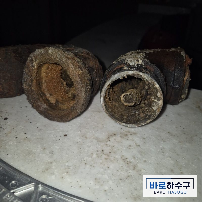 바닥에서 걷어낸 기존 주철 배관 단면, 녹과 찌꺼기가 관 안쪽을 두껍게 덮은 작업 전 상태